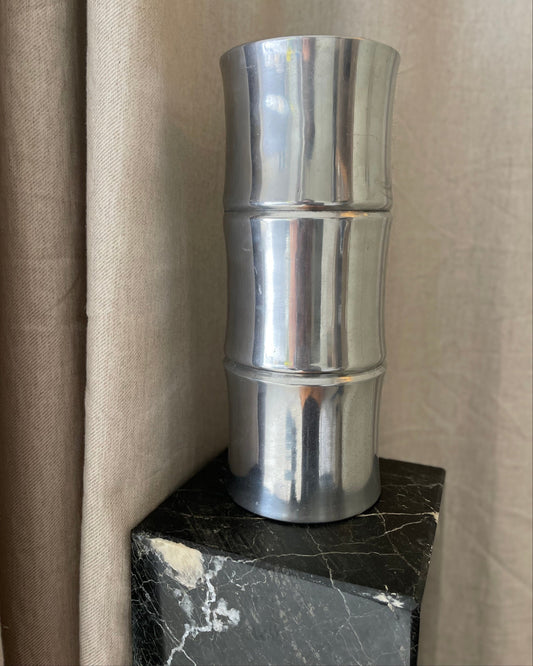 Metallic cylindrical object on a black surface with a beige curtain background