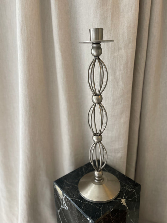 Decorative metal candlestick on a black marble base against a beige curtain background